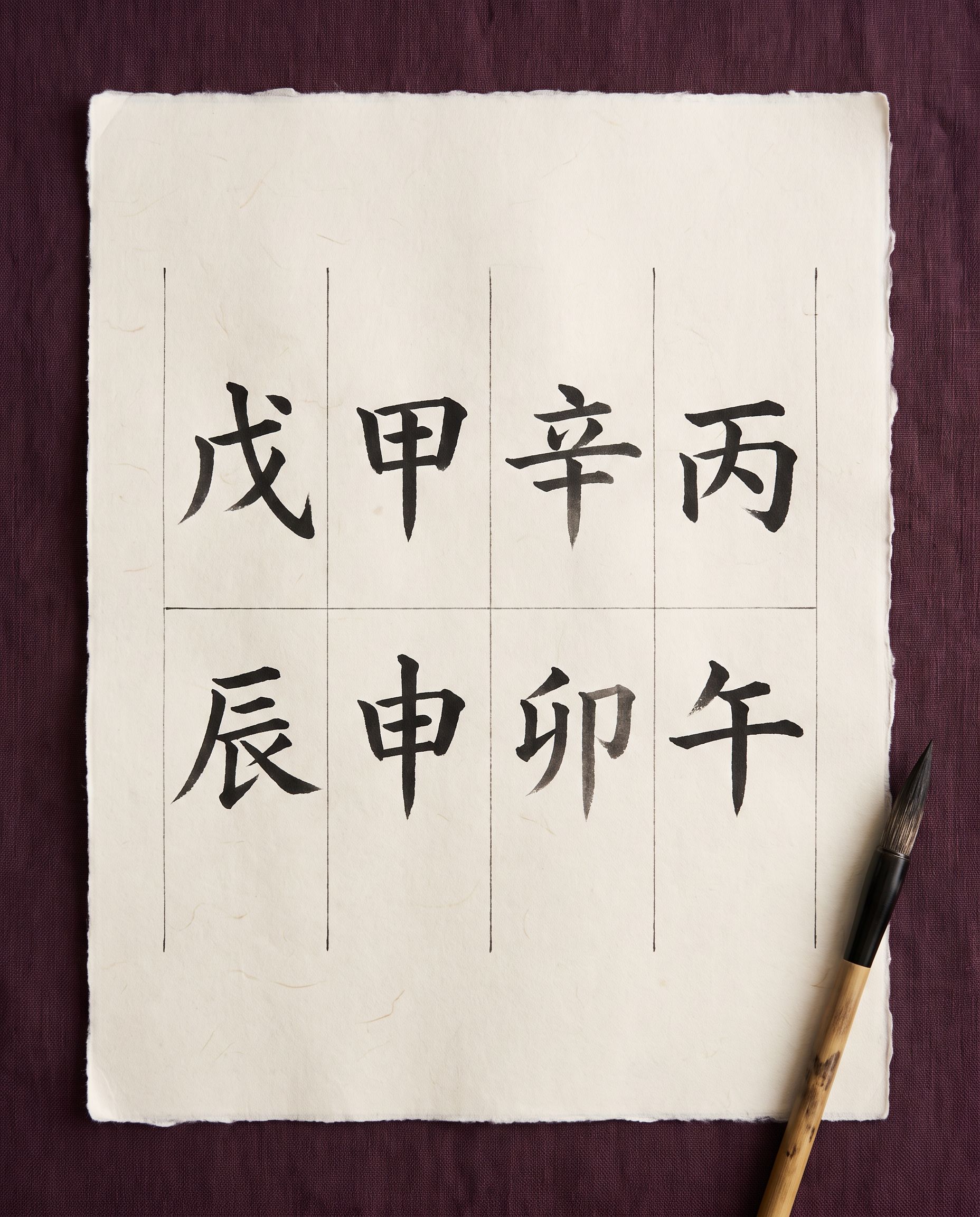 A BaZi chart of four pillars, brushed in black ink on cream paper, on a plum cloth